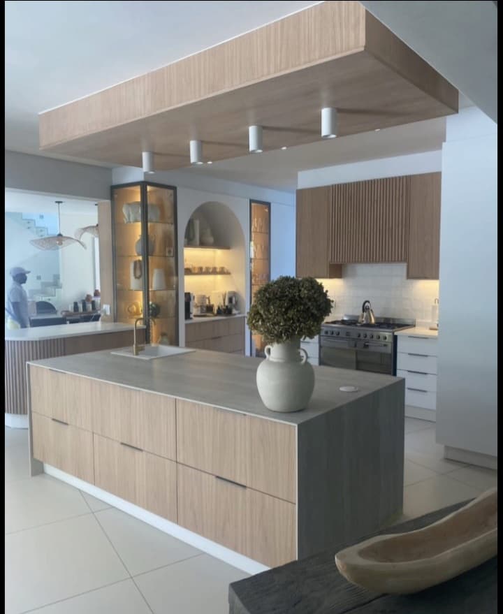 Modern kitchen featuring a light wood island, grey countertop, and matching wooden ceiling canopy.
