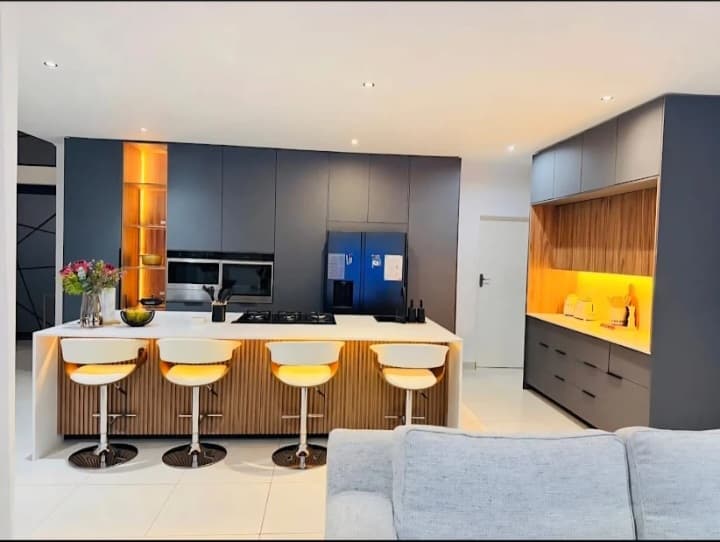 Modern kitchen featuring dark grey cabinets, wood accents, and a white island with stools.